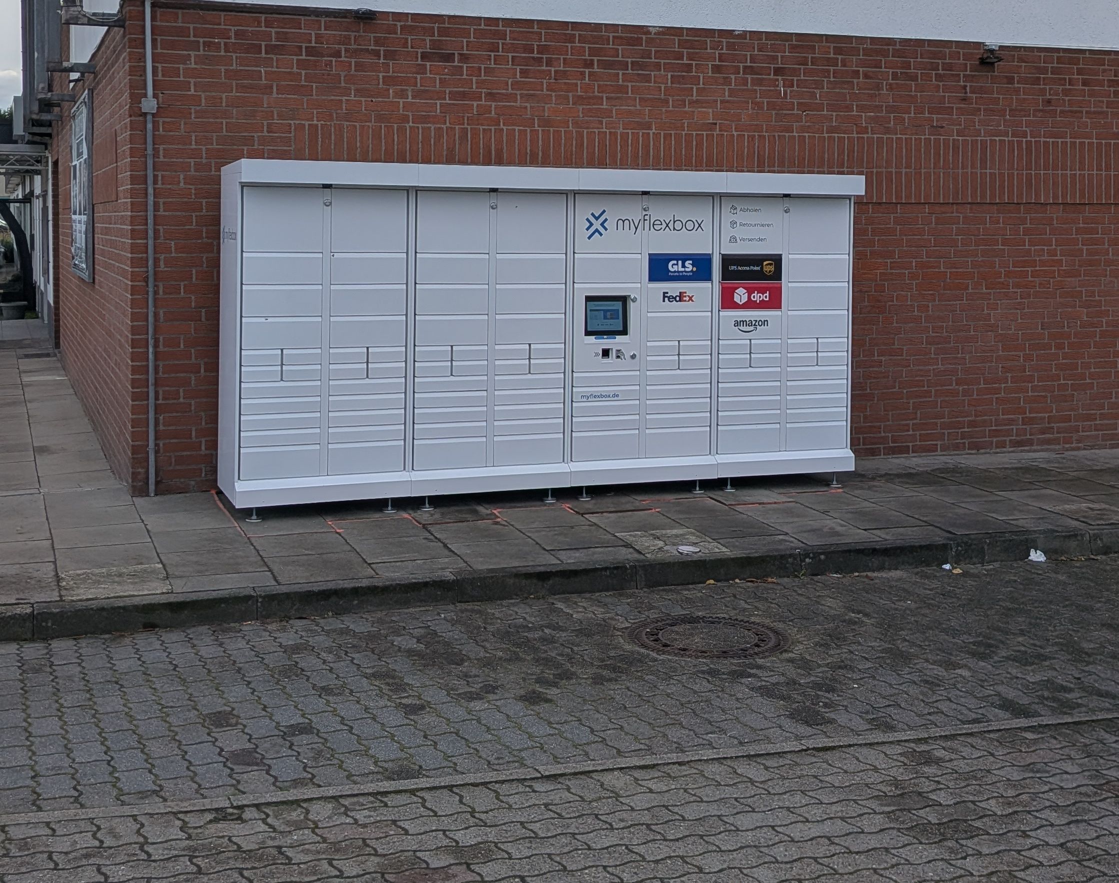 Die weiße 24/7-Box an der Backsteinwand im Delvenauweg 4, von der Straße aus gesehen
